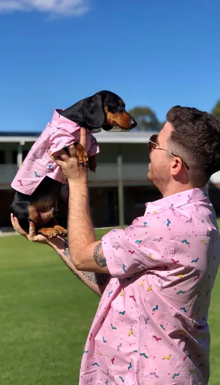 man lifting dachshund in pink matching shirt