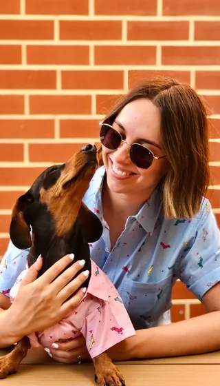 woman in blue dachshund shirt being kissed by her dog